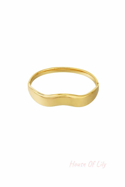 Minimalist wavy gold bangle bracelet with smooth polished surface against white background