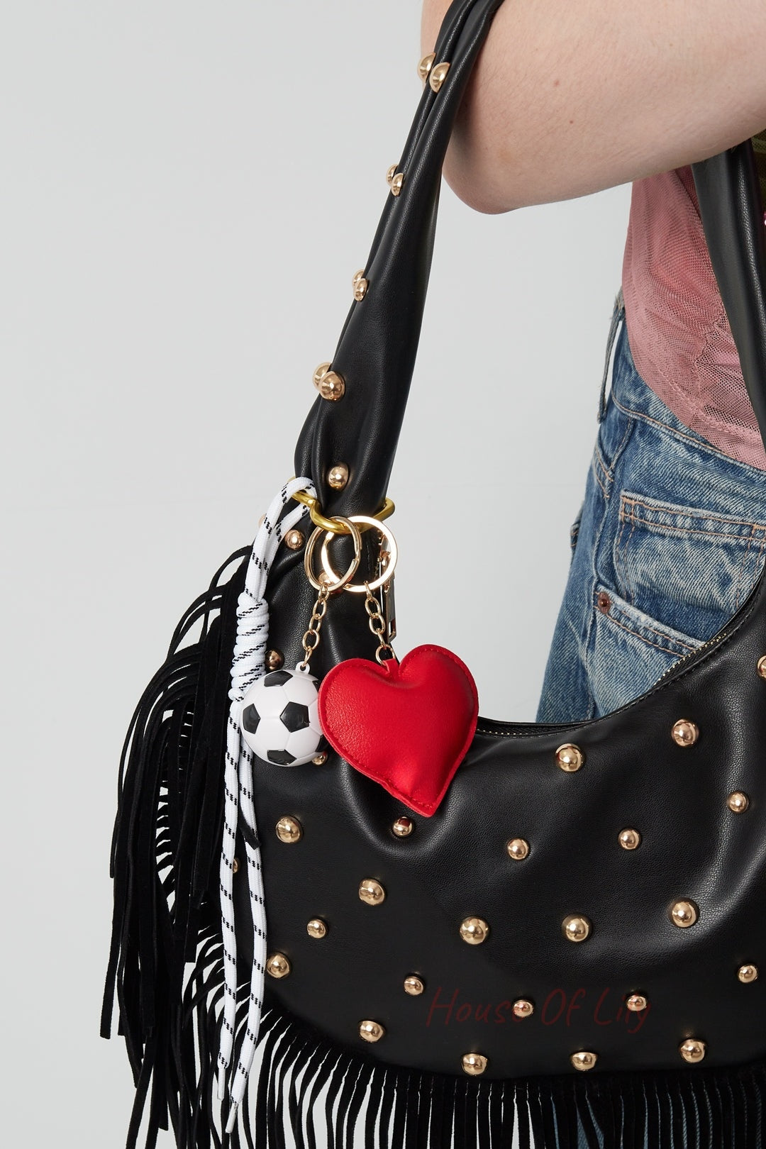 Woman carrying black studded leather bag with playful red heart and soccer ball bag charm attached on gold rings