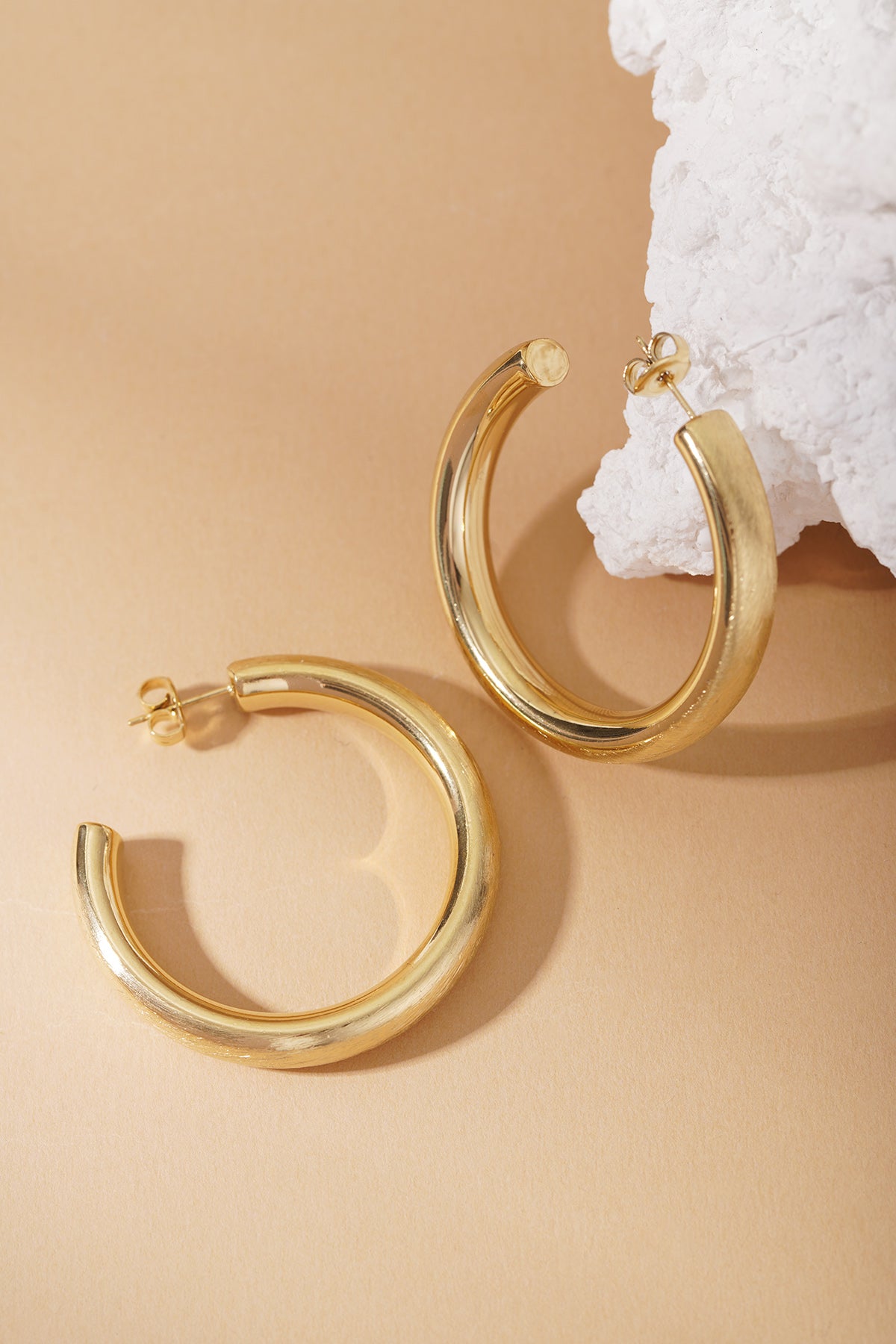 Mixed Metal Mood Hoops: Thick, polished gold-tone chunky hoop earrings on a beige background with a white stone accent.