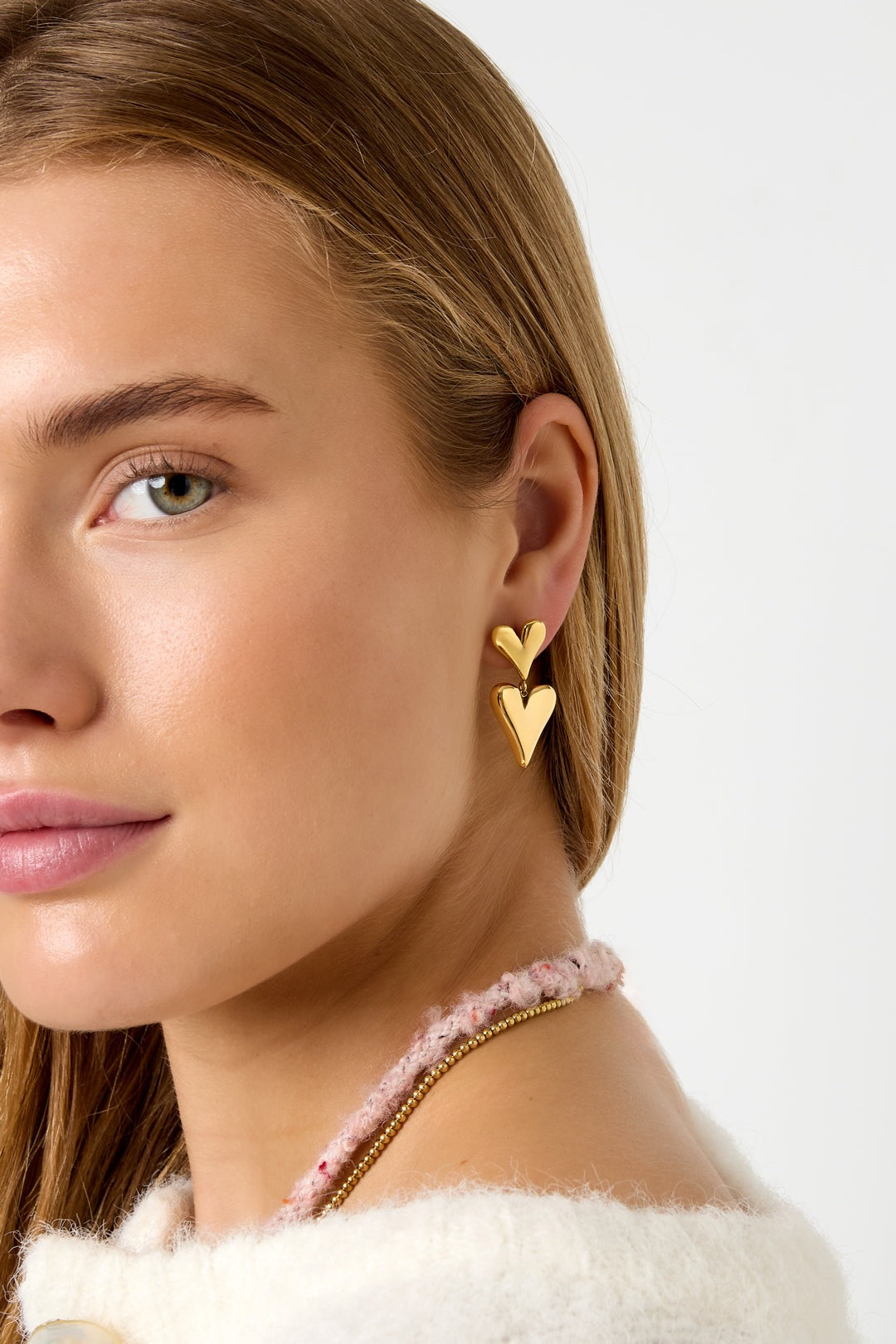 Close-up of woman wearing gold double heart drop earrings, showing how they dangle and complement her outfit