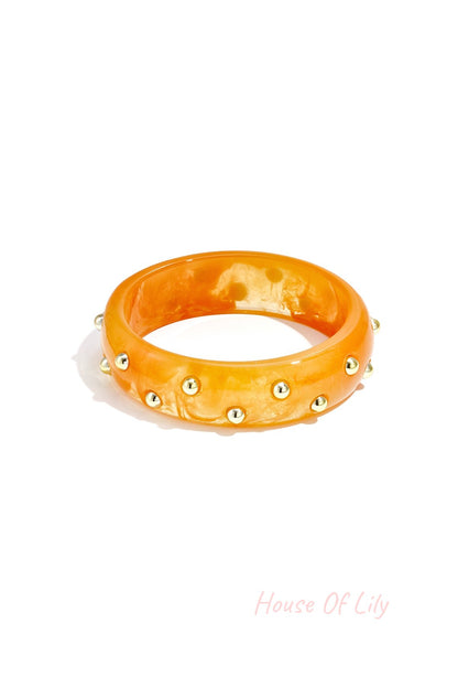 Orange resin bangle with gold-tone studs on white background