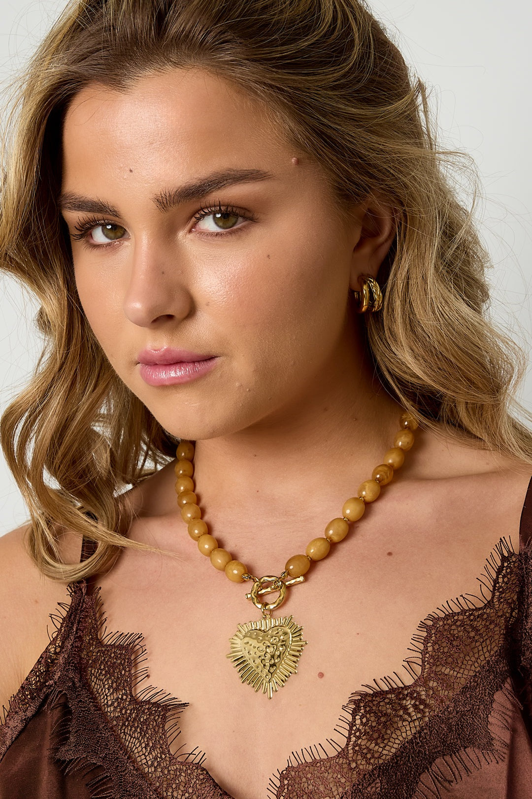model wearing nude beige beaded heart necklace with gold pendant styled with brown lace top