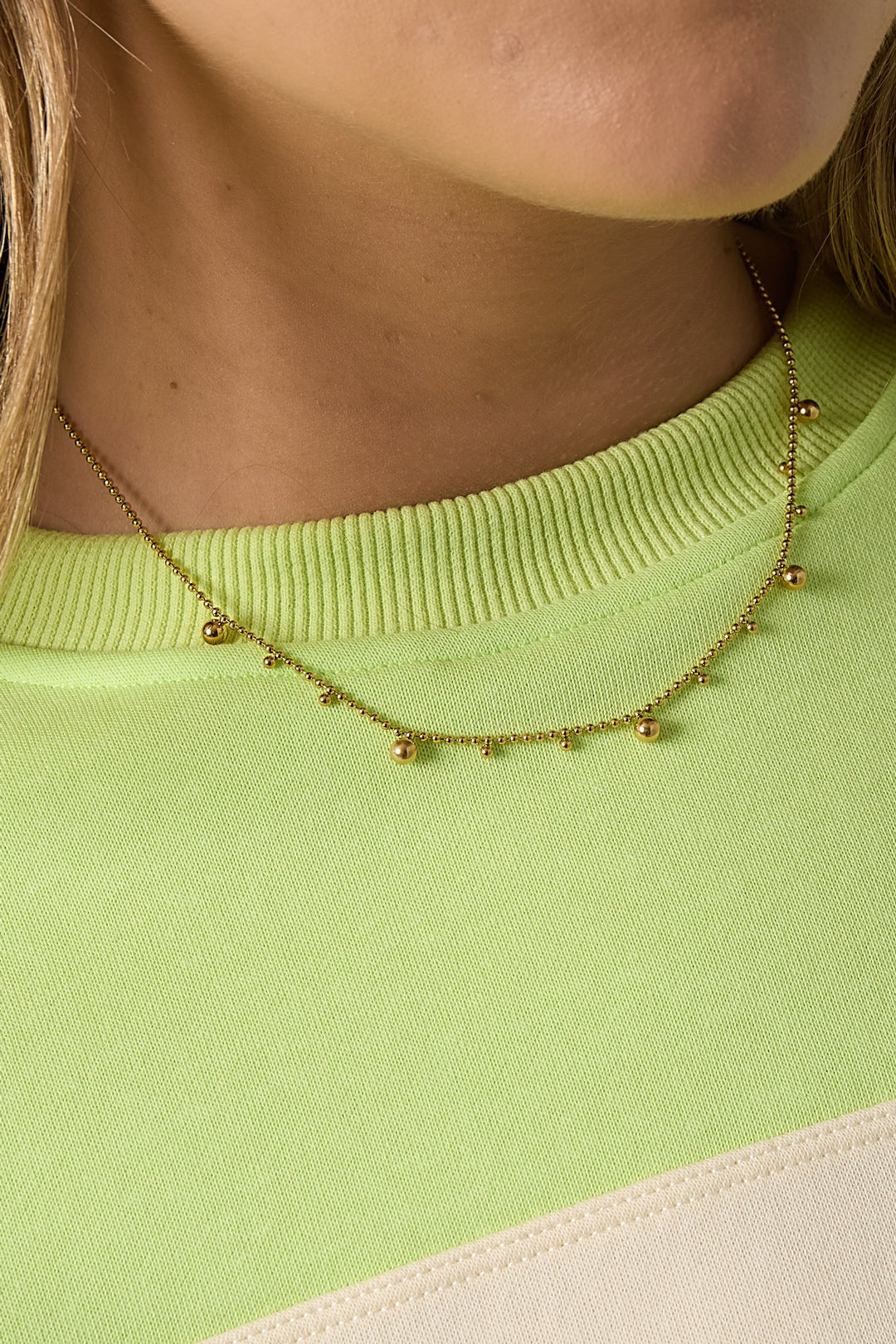 Close-up of the gold tone polka dot necklace on woman wearing lime green sweater, showing fine detailing of beads and chain