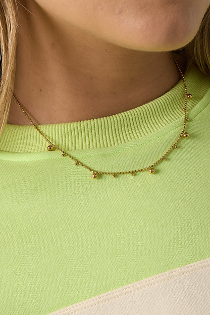 Close-up of the gold tone polka dot necklace on woman wearing lime green sweater, showing fine detailing of beads and chain