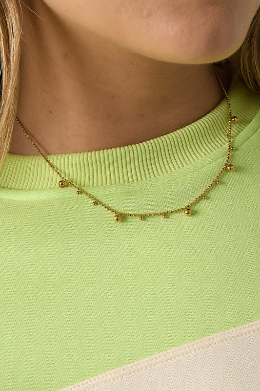 Close-up of the gold tone polka dot necklace on woman wearing lime green sweater, showing fine detailing of beads and chain