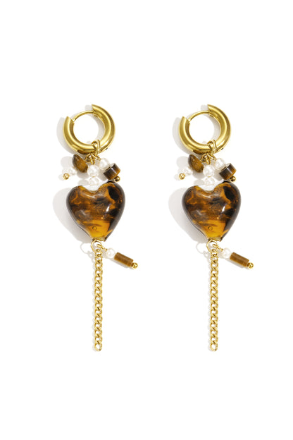 Pair of gold hoop drop earrings with amber tortoiseshell heart charms, faux pearls, and dangling gold chains against white background