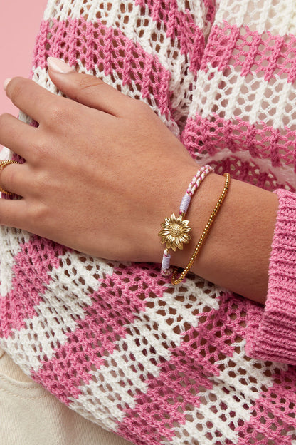 Close-up of pastel multicolor braided rope bracelet with gold flower charm on white background