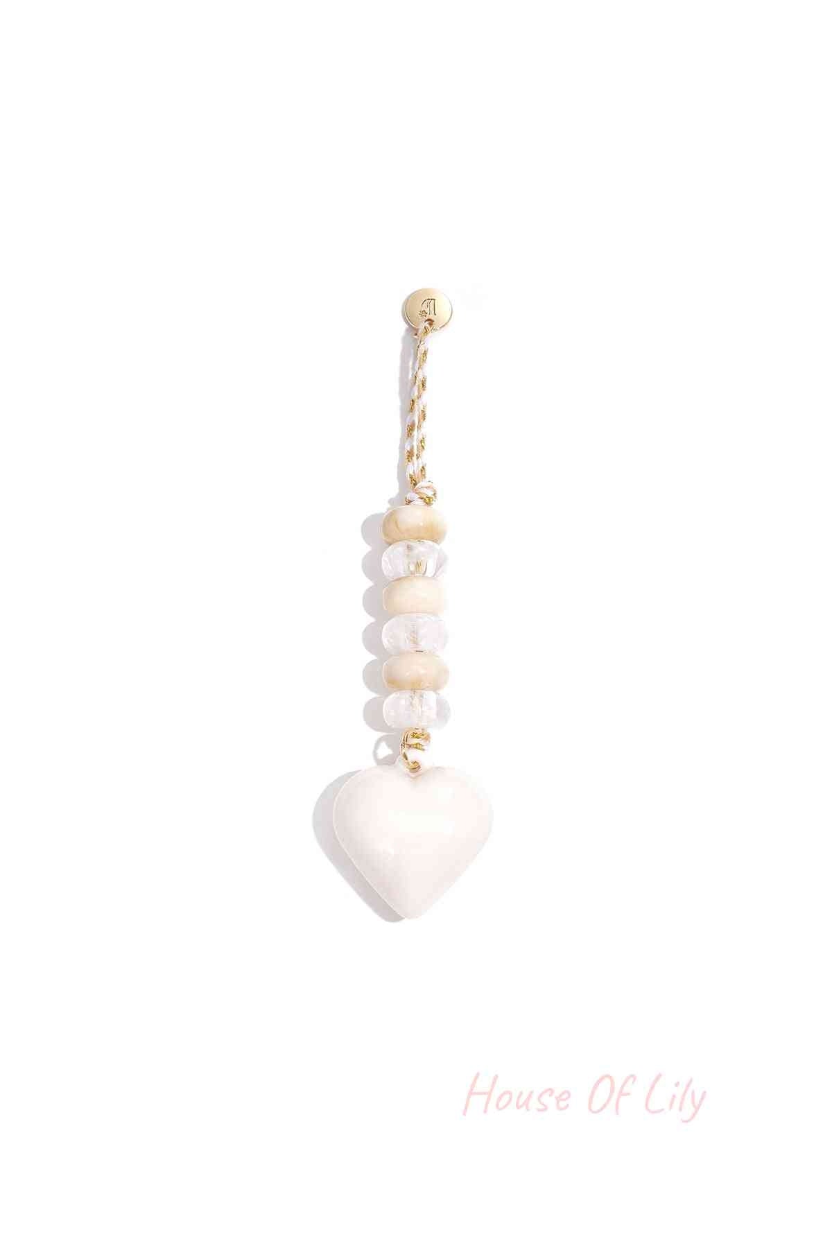 White heart-shaped acrylic bag charm with clear and ivory beads on white and gold braided loop hanging alone against white background.