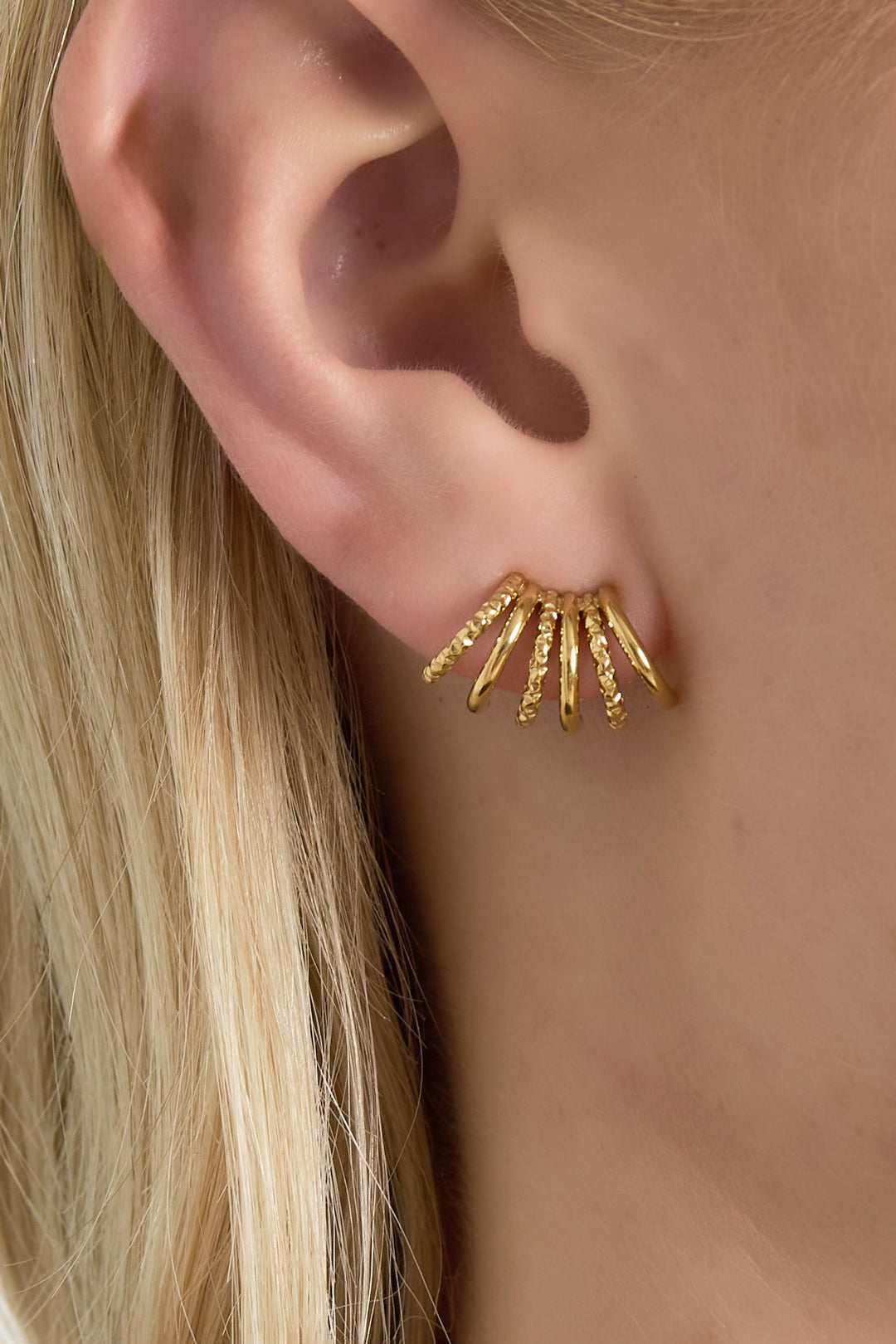 Close-up of gold textured fan stud earring worn on a woman's ear showing layered arc design