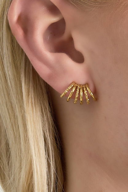 Close-up of gold textured fan stud earring worn on a woman's ear showing layered arc design