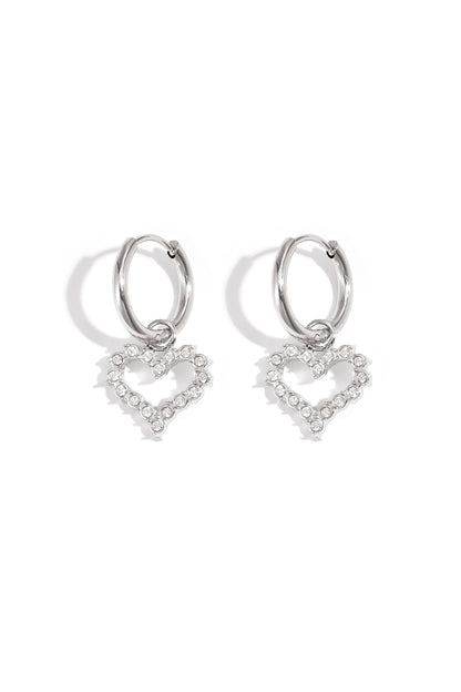Silver-tone hoop earrings with dangling heart-shaped rhinestone charms on white background