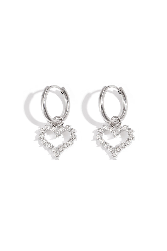 Silver-tone hoop earrings with dangling heart-shaped rhinestone charms on white background