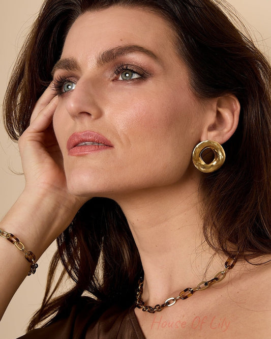 Close-up of woman wearing gold organic hoop stud earrings, styled with chain necklace and brown top