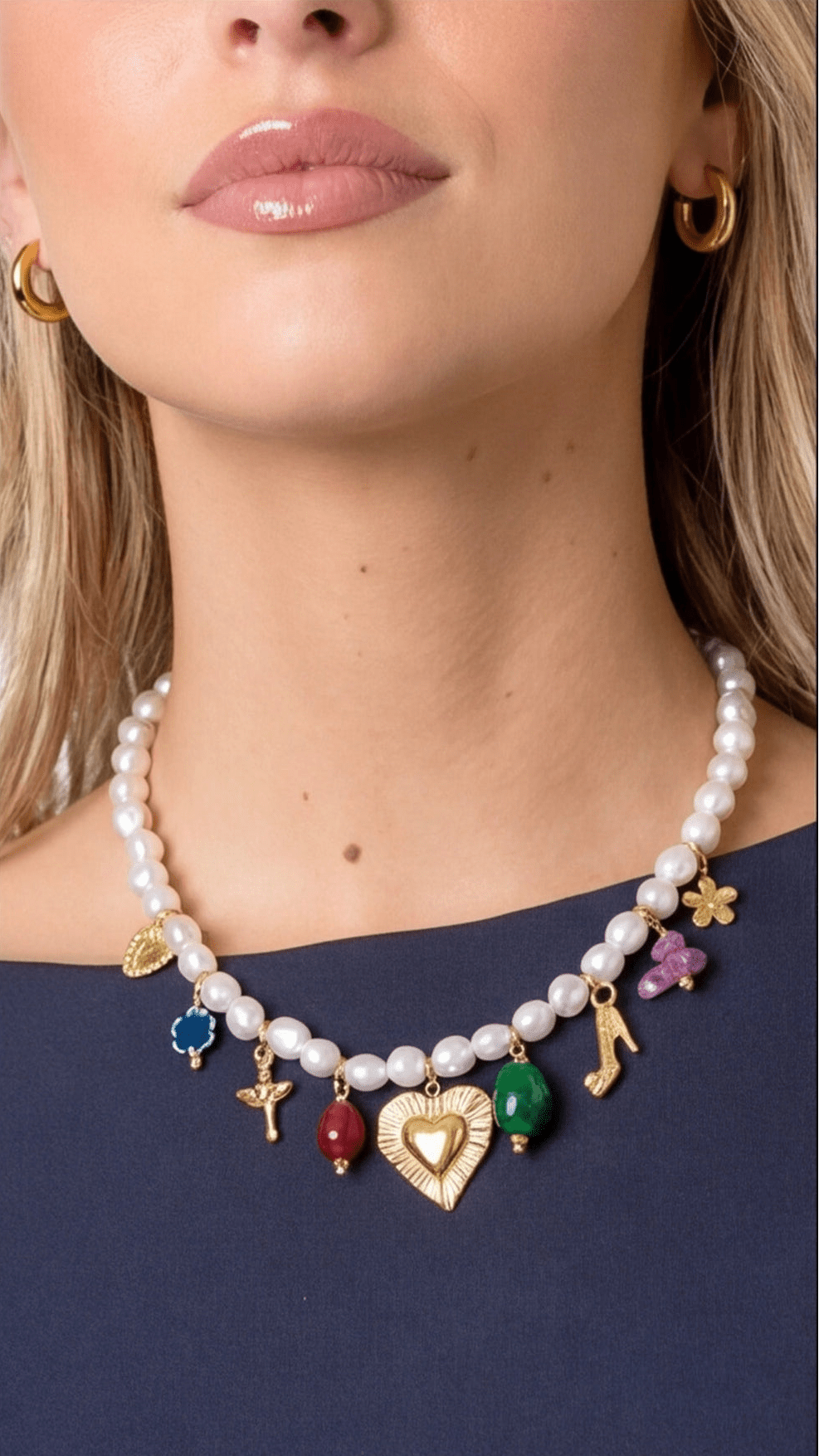 Pearl multi-charm necklace featuring varied gold charms, colorful gemstones, and a central heart pendant on a woman.