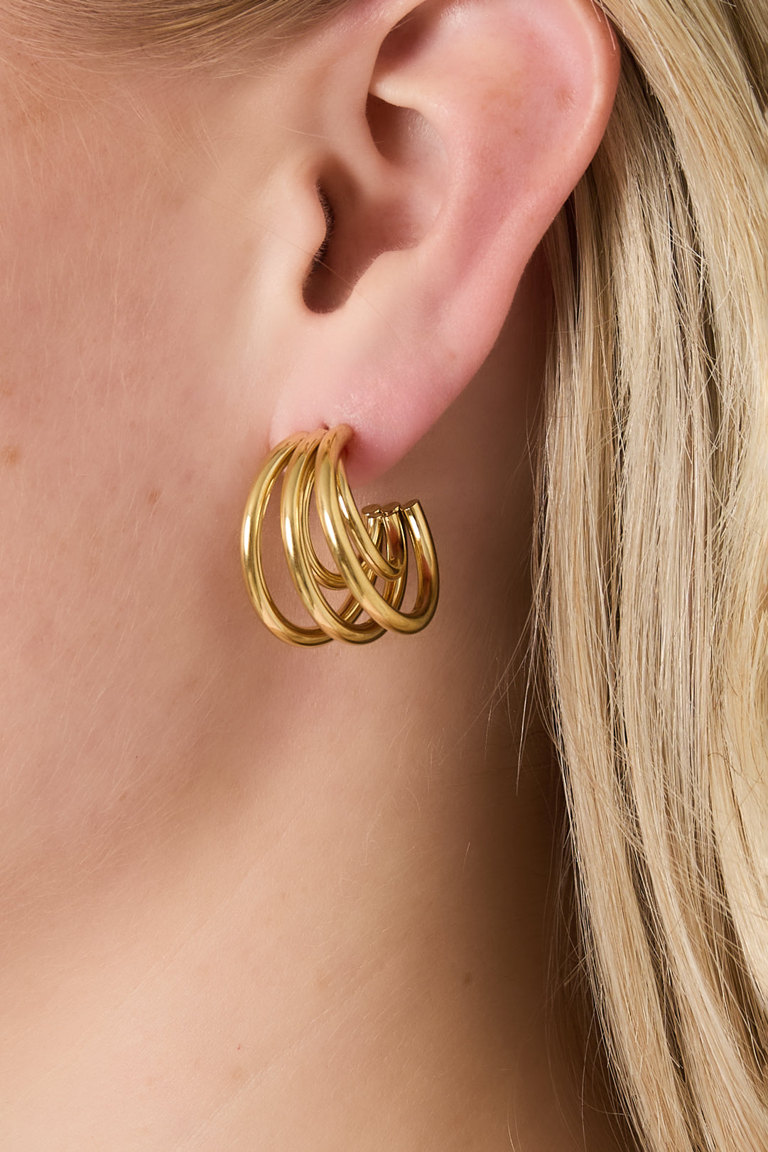 Close-up of a woman wearing gold triple hoop earrings highlighting their layered, elegant look