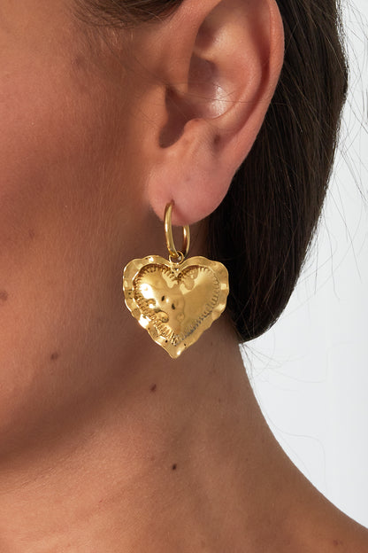 Close-up of a model wearing a gold heart drop hoop earring showing size and design