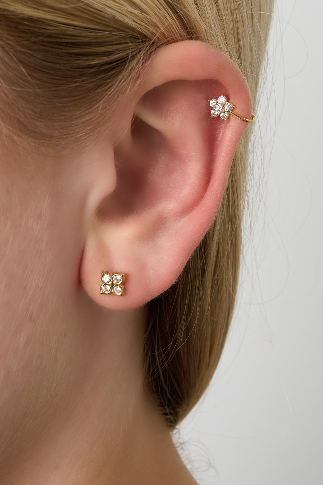 Woman’s ear wearing a gold floral ear cuff on the upper cartilage and matching small stud earrings on the ear lobe