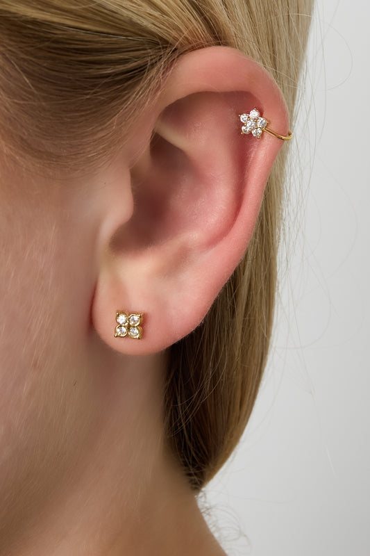 Woman’s ear wearing a gold floral ear cuff on the upper cartilage and matching small stud earrings on the ear lobe