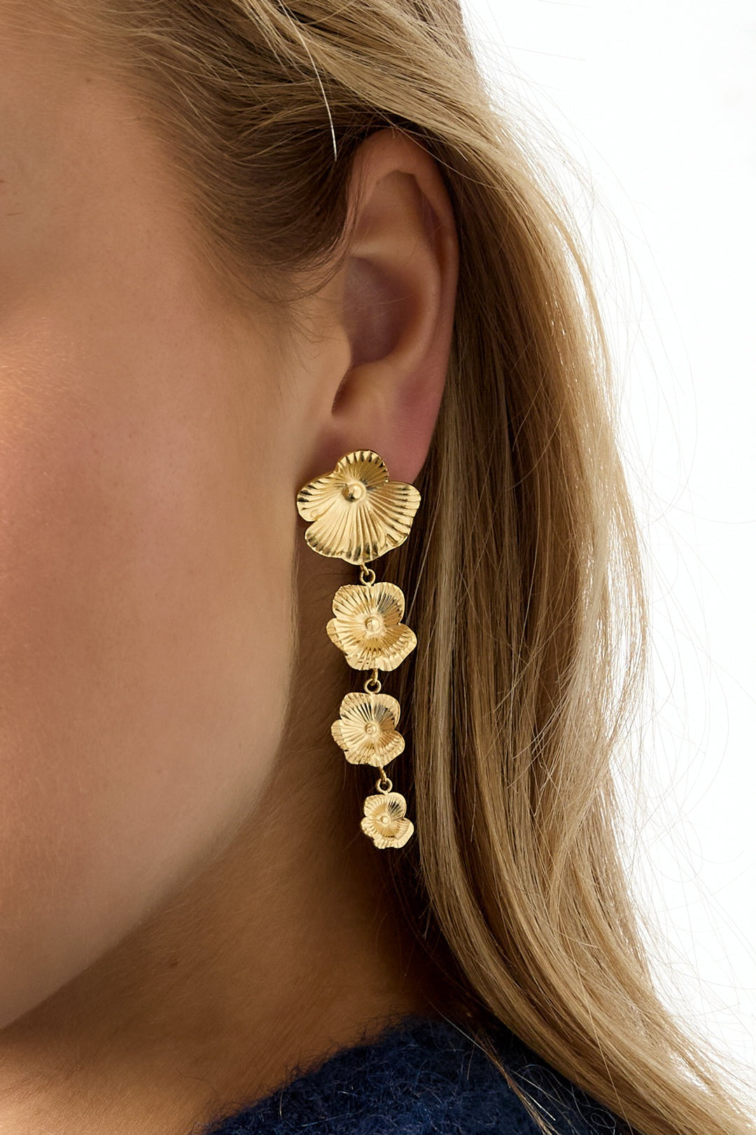 Close-up side view of model wearing gold floral cascade dangle earrings with blonde hair