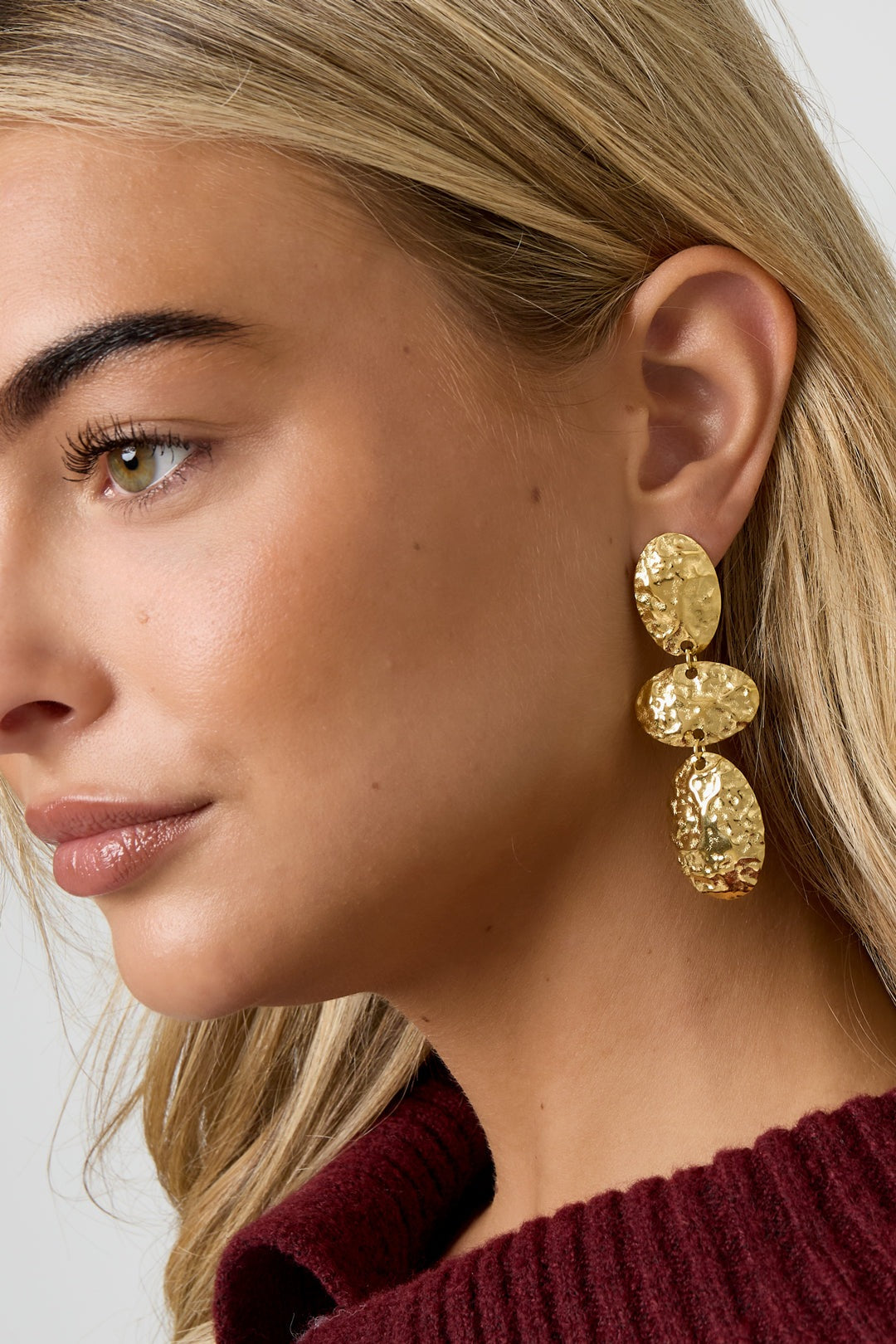 Close-up of model’s profile wearing hammered gold oval dangle earrings highlighting the textured, lightweight design