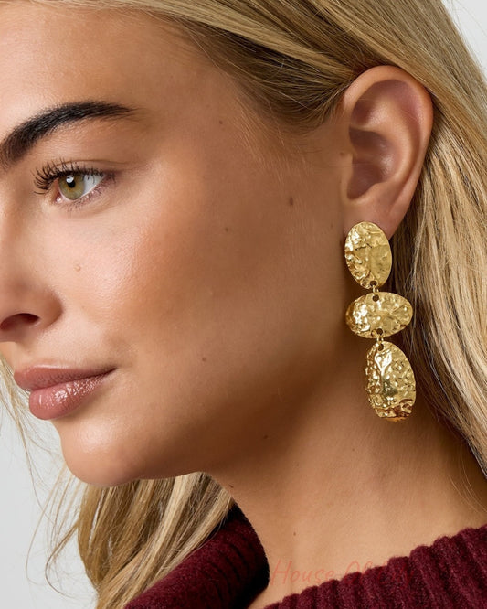 Close-up of model’s profile wearing hammered gold oval dangle earrings highlighting the textured, lightweight design