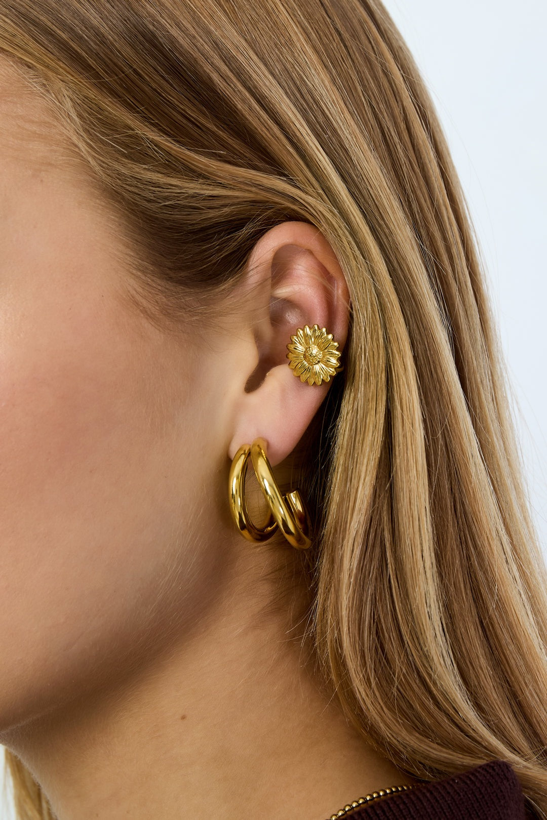 Woman wearing gold flower-shaped ear cuff and matching gold hoop earrings on ear