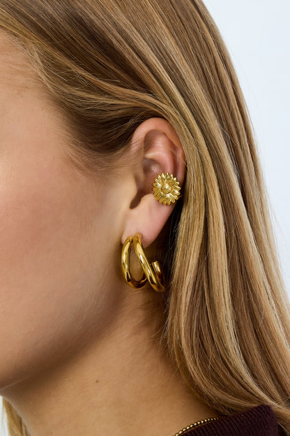 Woman wearing gold flower-shaped ear cuff and matching gold hoop earrings on ear