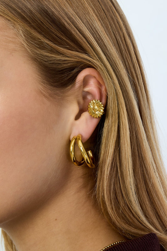 Woman wearing gold flower-shaped ear cuff and matching gold hoop earrings on ear