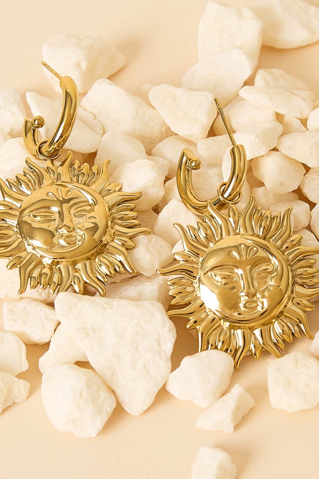 Close-up of gold sun face drop earrings laying on white decorative stones