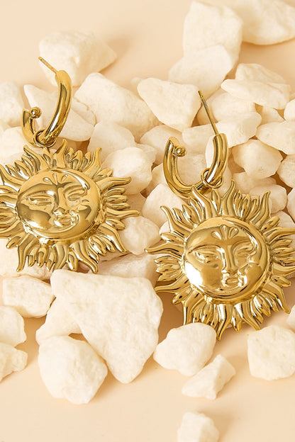 Close-up of gold sun face drop earrings laying on white decorative stones