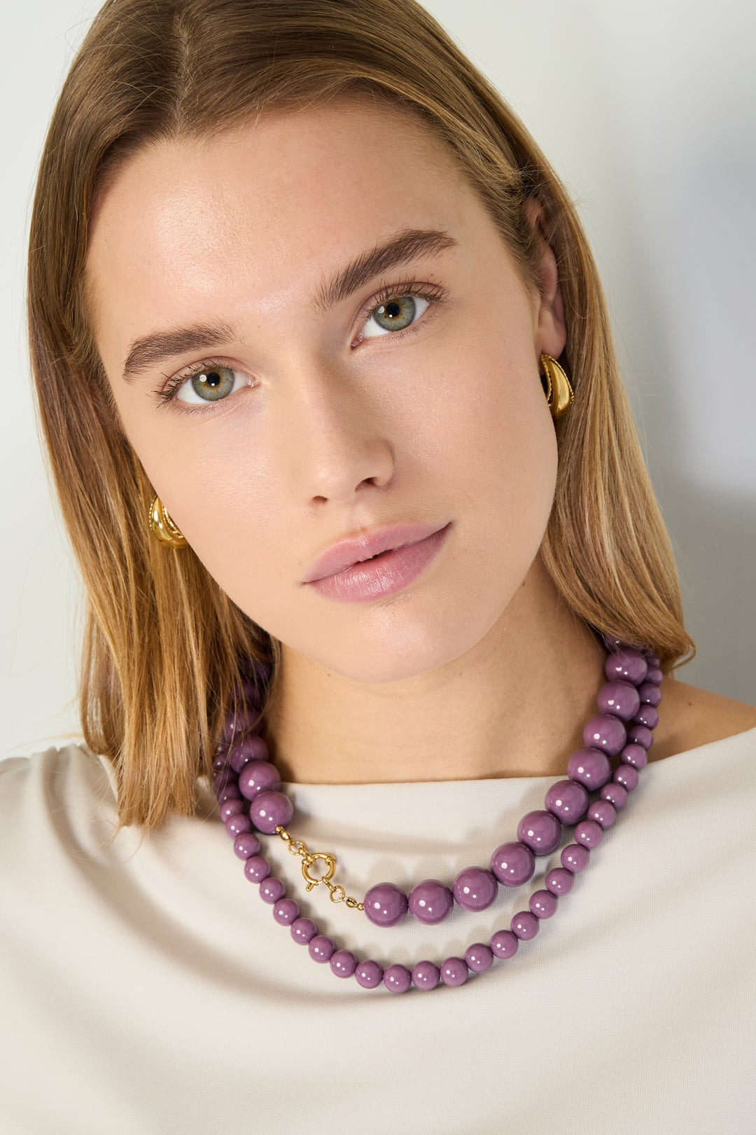 Model wearing layered purple resin beaded necklaces with gold clasp and gold hoop earrings
