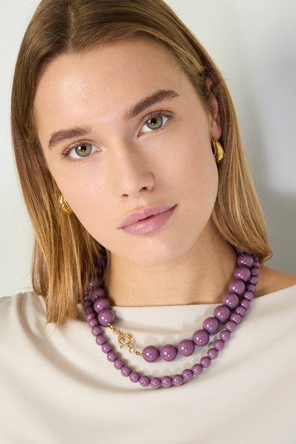Model wearing layered purple resin beaded necklaces with gold clasp and gold hoop earrings