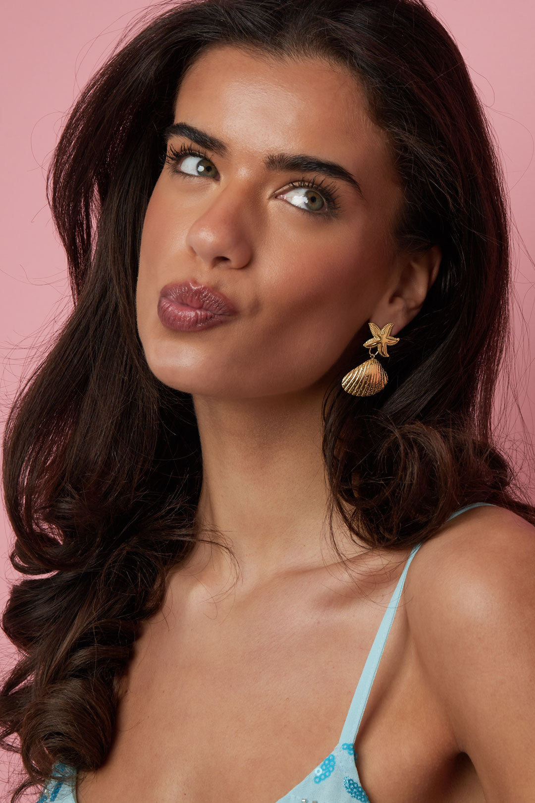 Close-up of model wearing gold starfish and shell earrings showing delicate detail