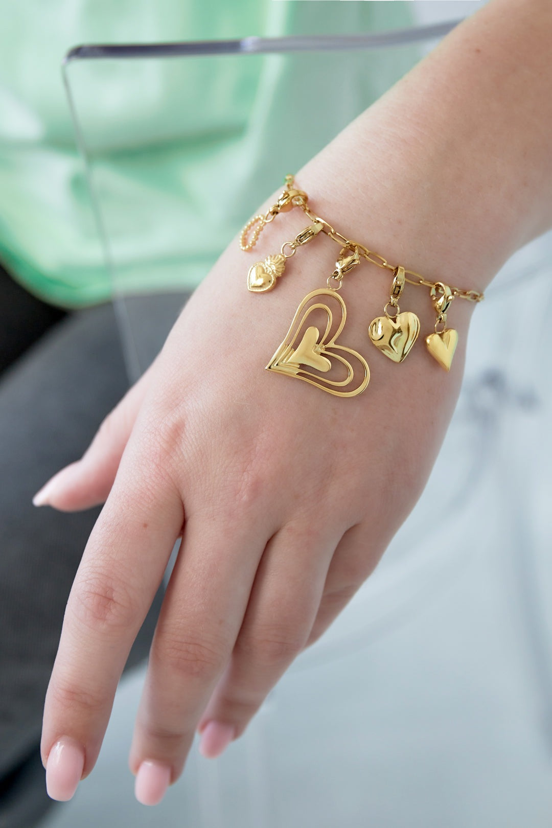Gold heart charm bracelet worn on a wrist, showing the playful dangling heart charms and adjustable paperclip chain