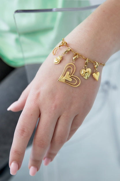 Gold heart charm bracelet worn on a wrist, showing the playful dangling heart charms and adjustable paperclip chain
