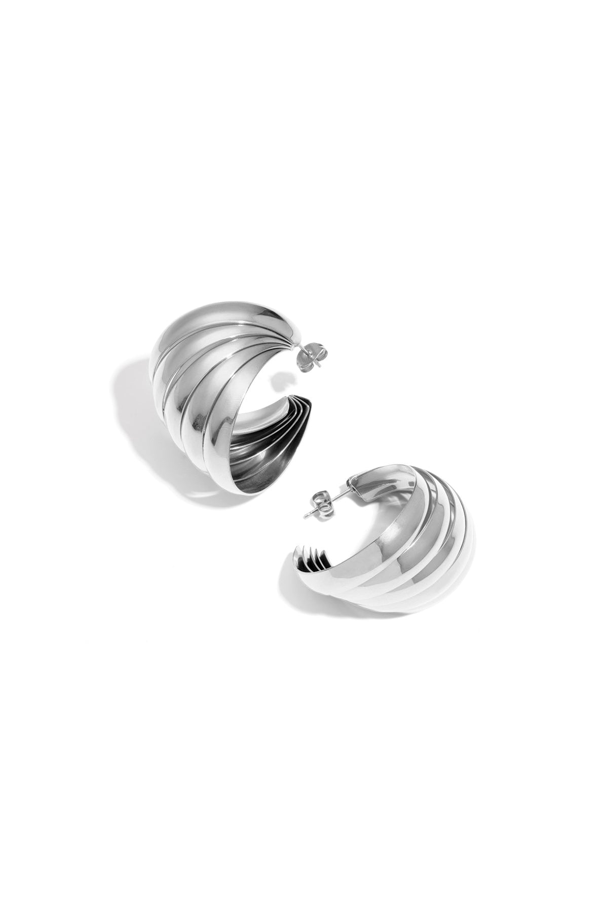 Pair of sculpted hoop earrings with layered ripples in polished silver finish on white background