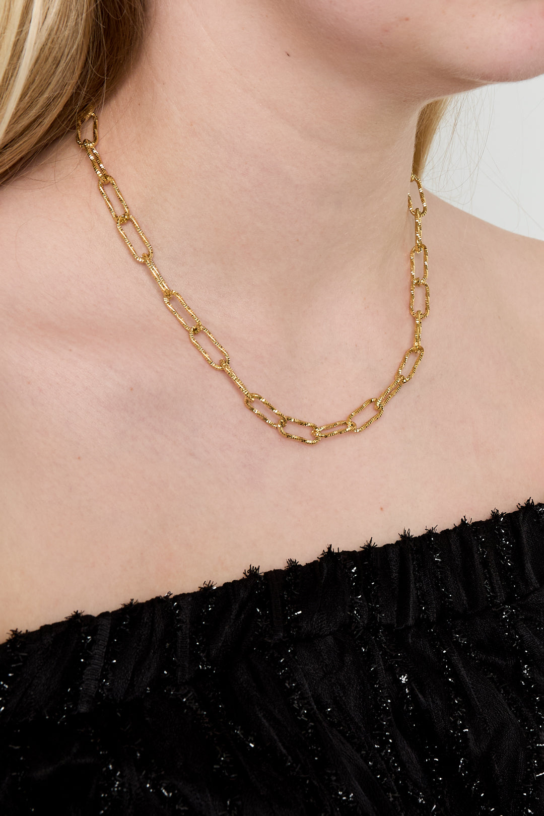 Simple gold textured link chain necklace worn close-up on a woman in black top