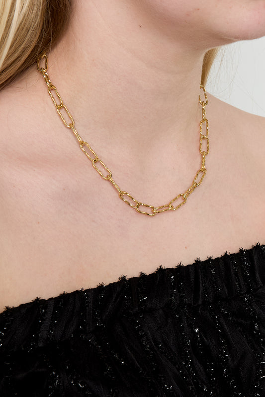 Simple gold textured link chain necklace worn close-up on a woman in black top