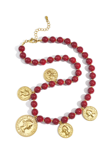 Crimson red acrylic beaded necklace with gold-tone vintage coin pendants laid flat on white background