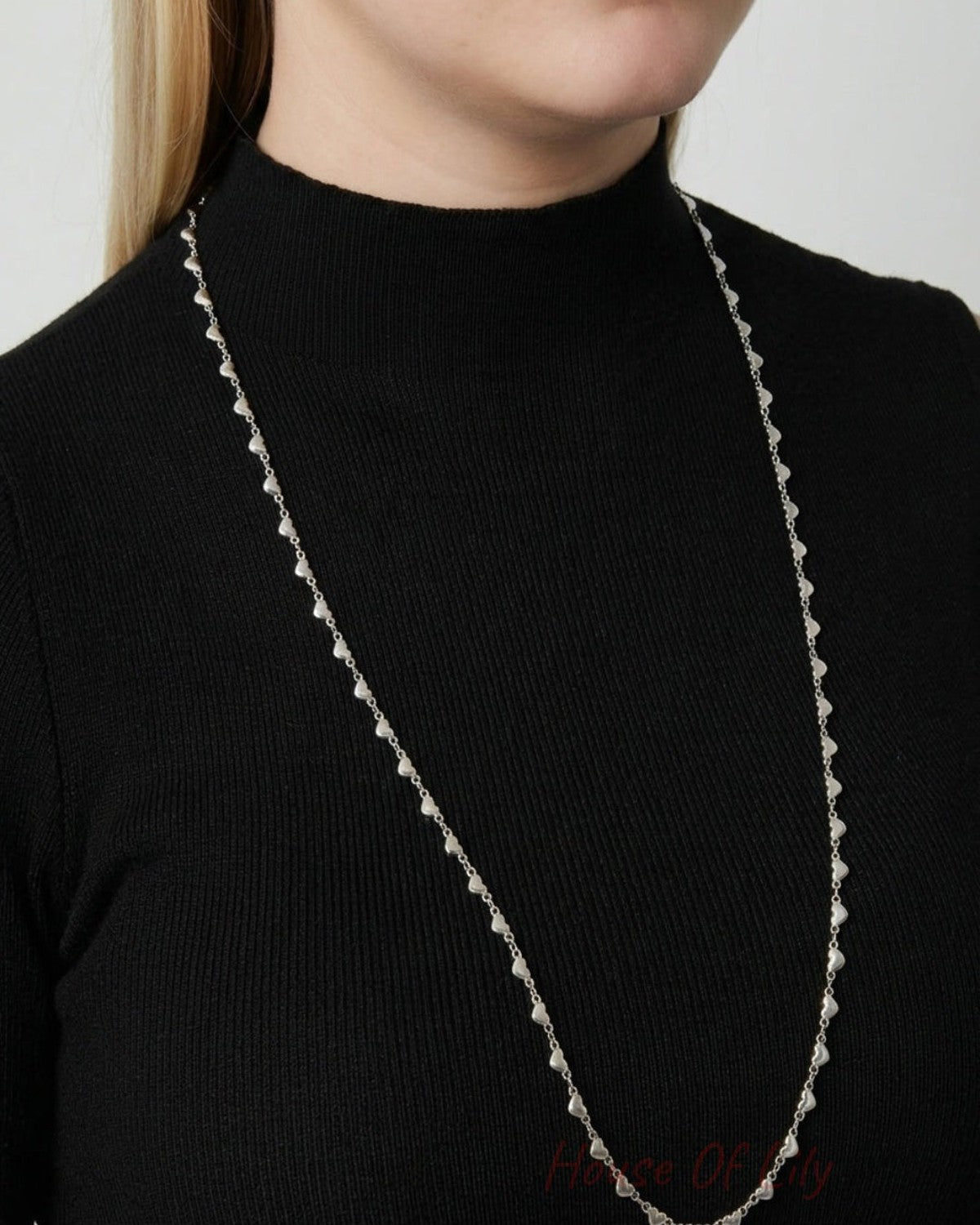 A long silver metal necklace featuring a delicate chain of evenly spaced tiny hearts.