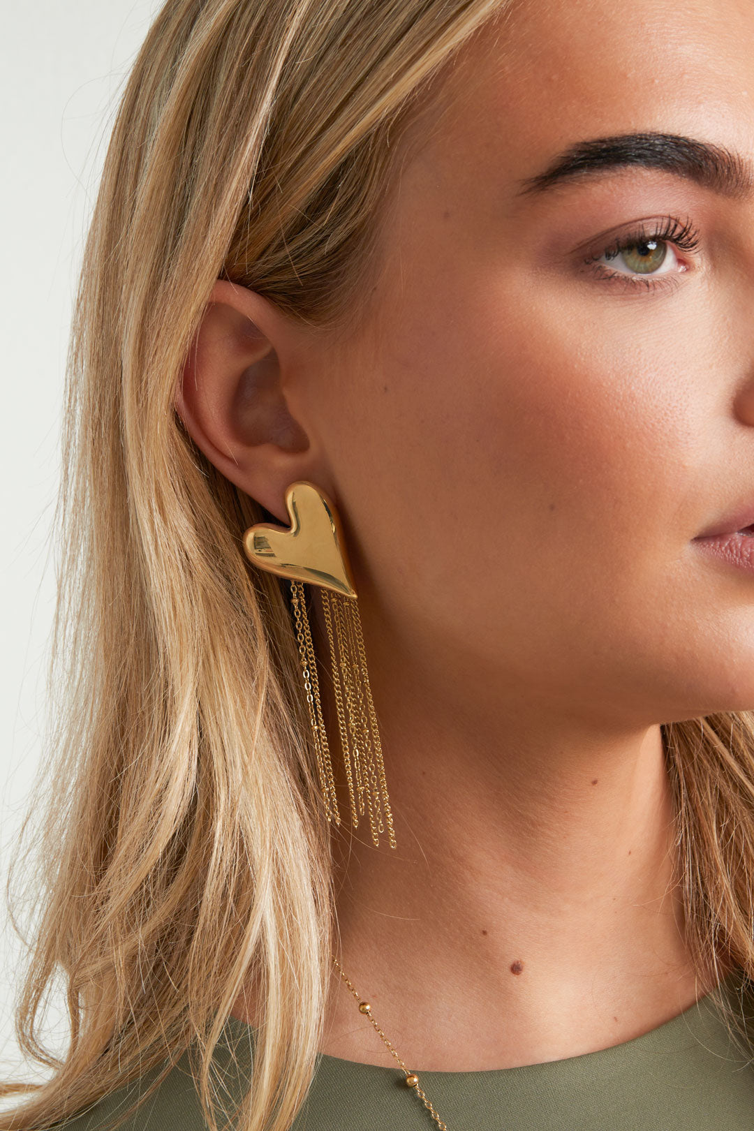 Side view of woman wearing golden heart chain tassel earrings showcasing their size and style