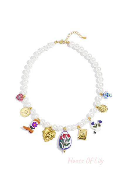 Pearl necklace with various colorful and gold-tone charms including hearts, flowers, coin, and envelope on white background