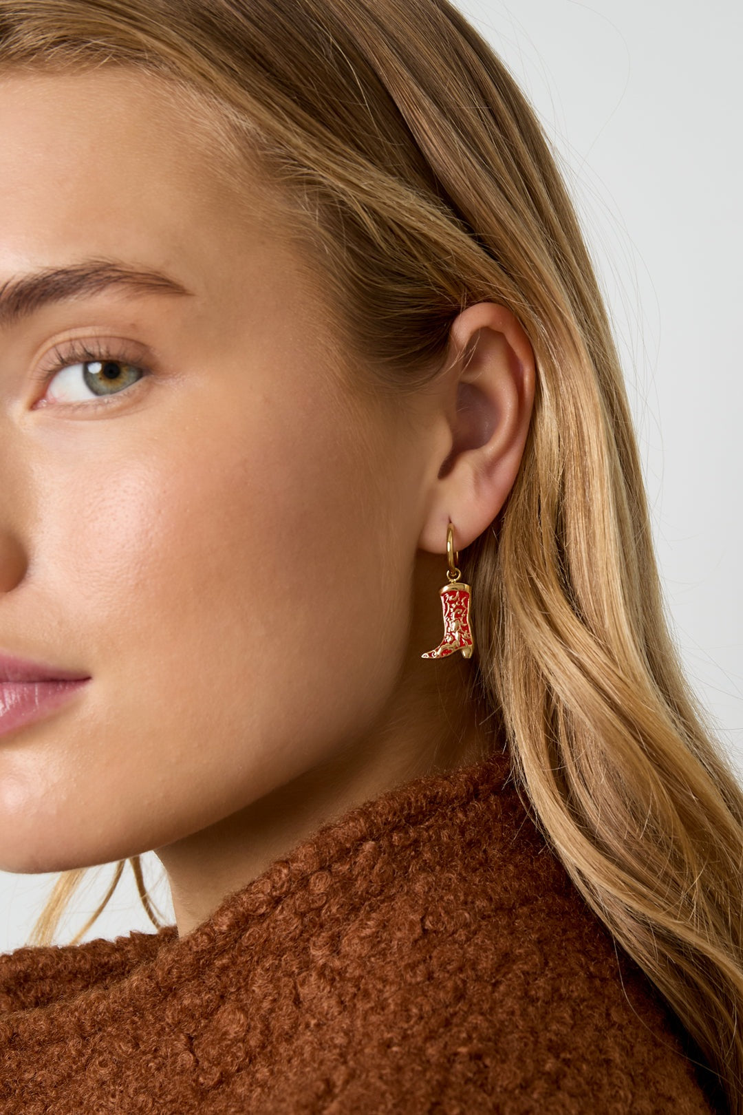 Close-up of woman wearing one gold-tone red enamel cowboy boot drop earring, side profile