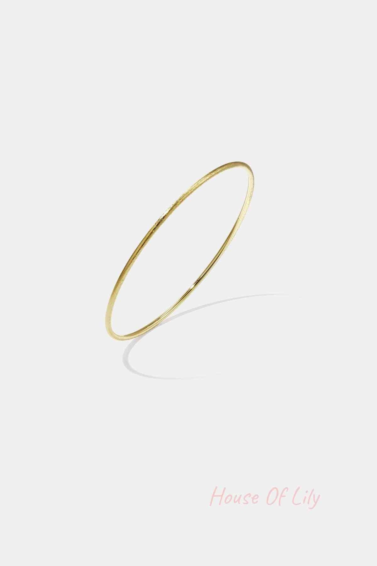 Thin minimalist gold bangle bracelet on white background with shadow
