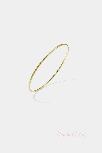 Thin minimalist gold bangle bracelet on white background with shadow