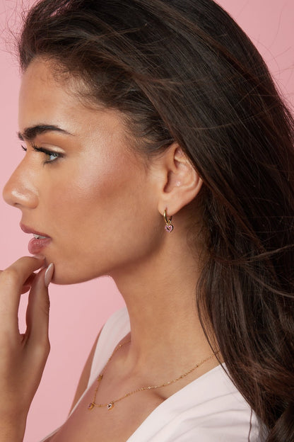 Model wearing Main Character Heart Hoops: small gold huggie hoops with delicate pink crystal heart charms.