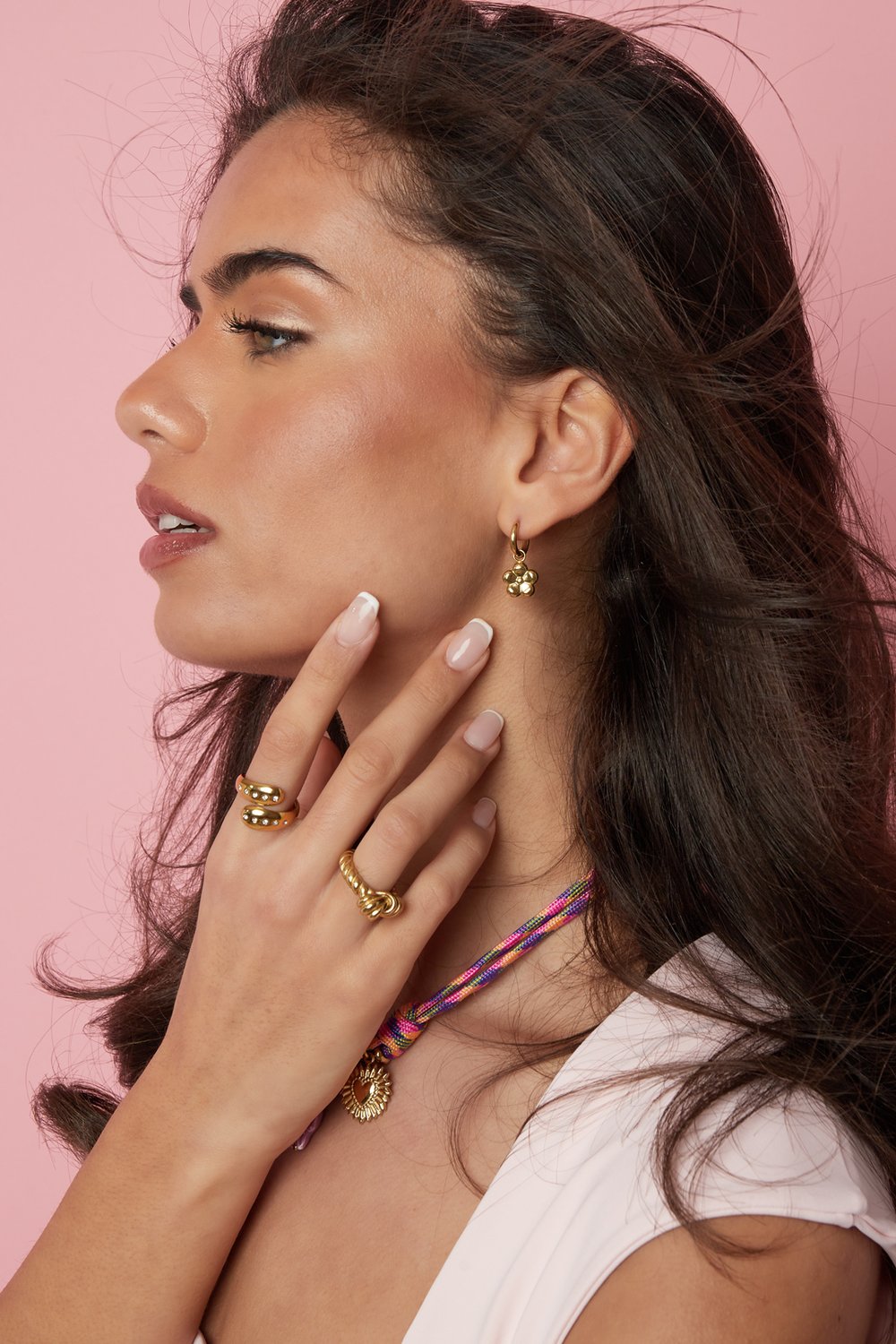 Model wearing gold Bloom Core Drip jewelry: a flower earring, two chunky gold rings, and a heart pendant on rope chain.