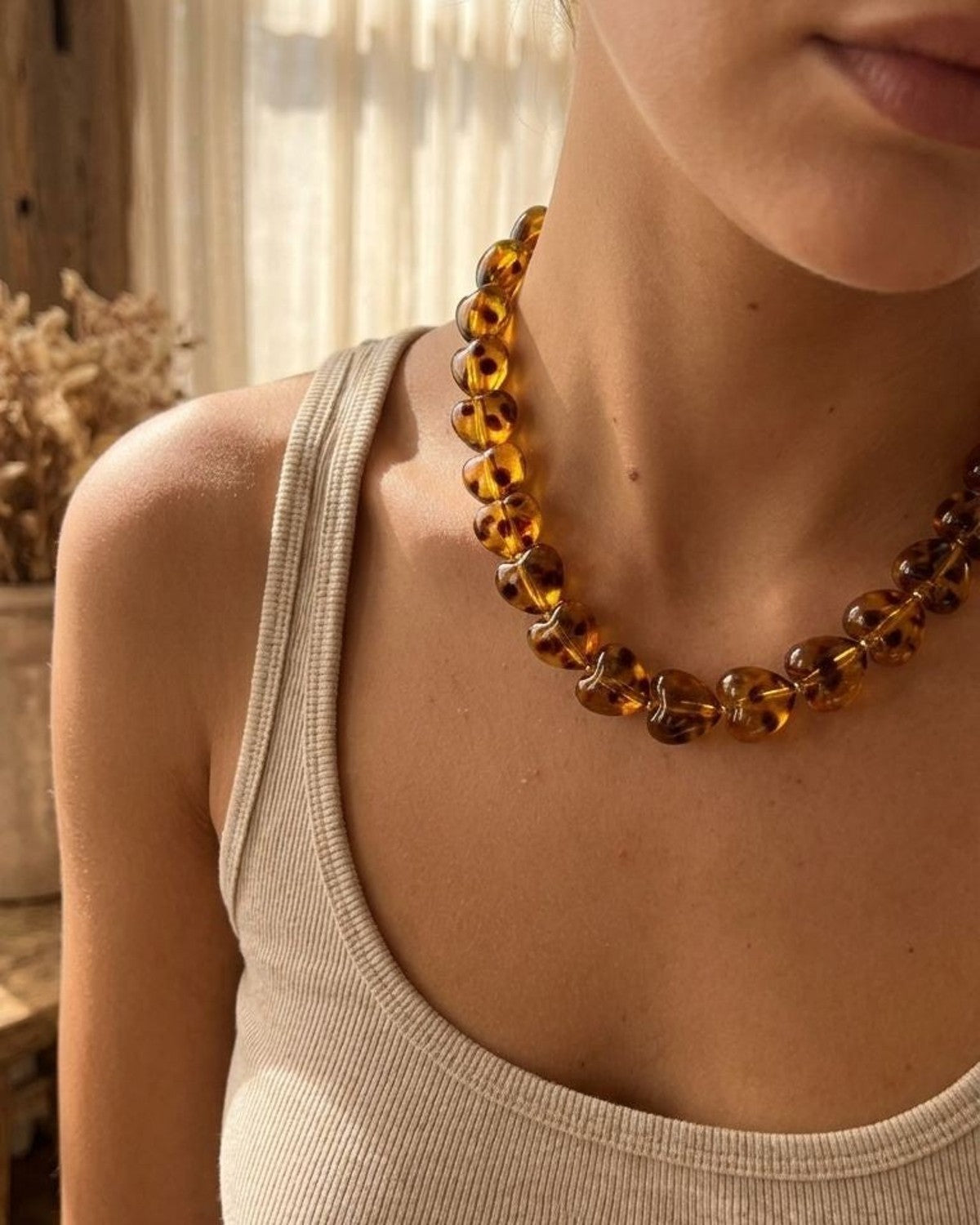 Delicate amber heart beaded necklace with gold clasp on a model's neck in warm natural sunlight, highlighting vintage charm and elegance.