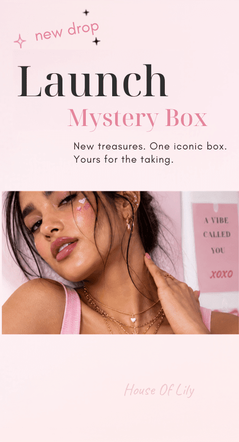 A woman wearing layered gold necklaces, hoop earrings, and a pink top against a pink backdrop.