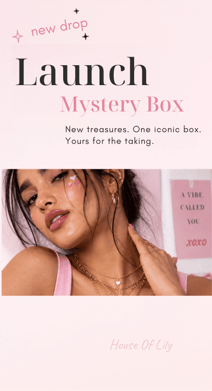 A woman wearing layered gold necklaces, hoop earrings, and a pink top against a pink backdrop.
